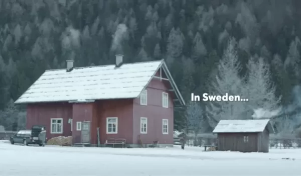 Rödmålad stuga i vinterlandskap med texten "In Sweden"